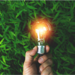 Sustainability image. Person holding lightbulb in front of a green background